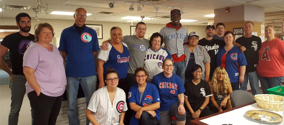 A diverse group people posing indoors, many wearing baseball jerseys.