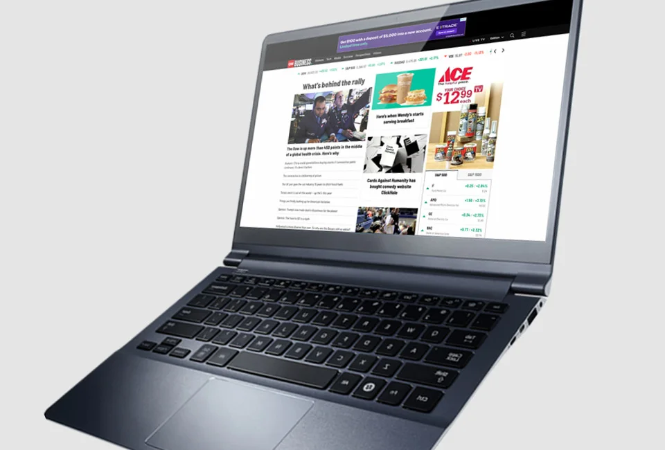 A laptop displaying a webpage with news articles and an advertisement against a gray background.