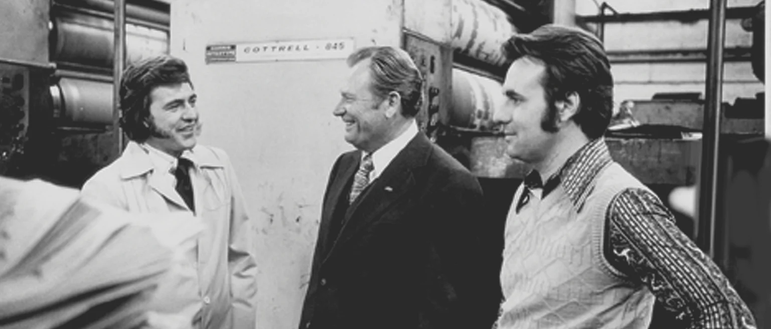 Three men in an industrial setting, standing near machinery
