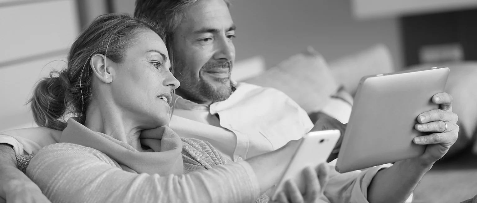 A couple sitting on a couch, engaged with a tablet and smartphone.