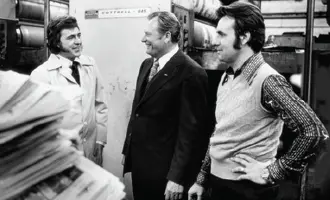 Three men in an industrial setting, standing near machinery